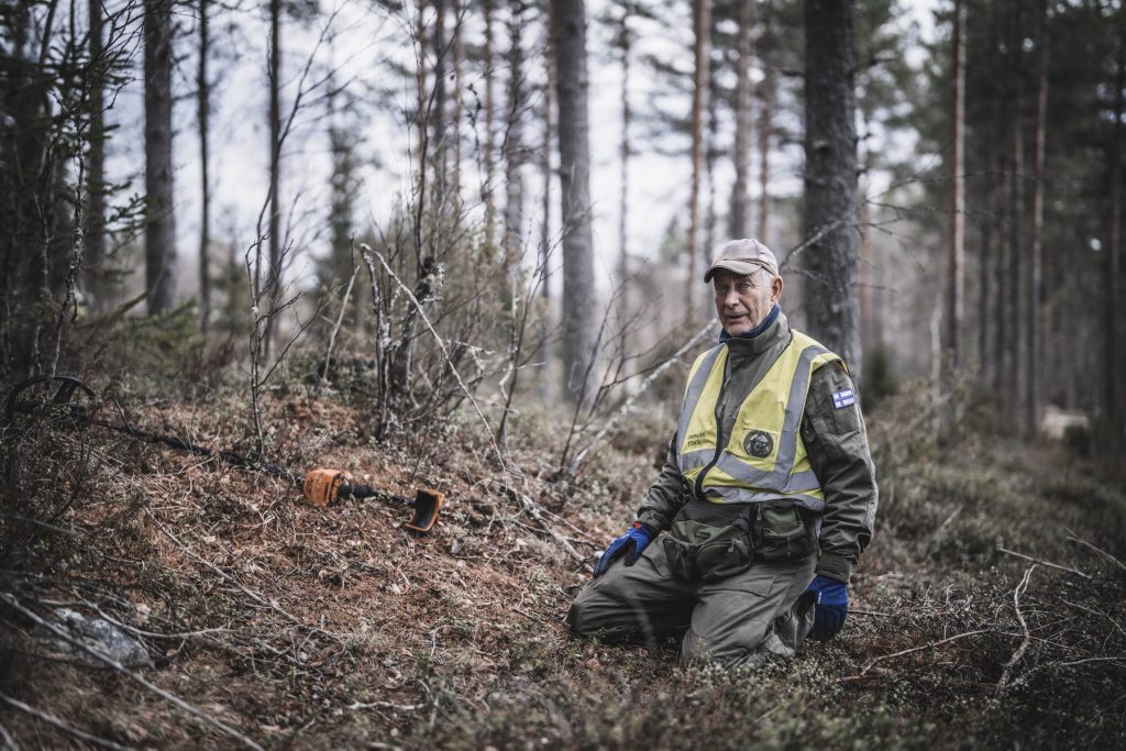 Etsijä on polvillaan metsässään ja katsoo kohti kameraa.